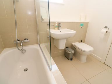 A bathroom with a bathtub a wall-mounted sink a toilet a trash bin and a toilet paper holder at Una Lodge 77 in Carbis Bay