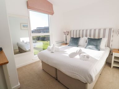 A bedroom with a bed with white linens and blue pillows next to a window showing a garden at Una Lodge 77 Carbis Bay