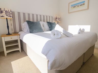 A bedroom with a bed with two pillows and rolled towels on it a bedside table with a lamp and a framed picture on the wall at Una Lodge 77 in Carbis Bay