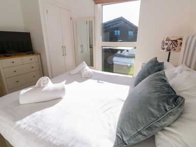 A bedroom with a bed with pillows and towels next to a window with a dresser and a tv at Una Lodge 77 Carbis Bay