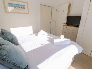 A bedroom with a bed with pillows and towels a dresser with a television and framed artwork on the wall at Una Lodge 77 in Carbis Bay