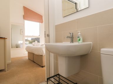 A bathroom sink with soap dispenser and a toilet next to a bedroom with a bed and a window at Una Lodge 77 in Carbis Bay