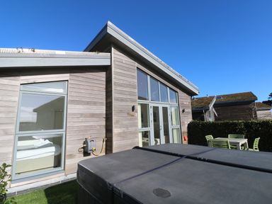 Exterior view of a wooden house with large glass doors and windows a covered hot tub and outdoor seating at Una Lodge 77 in Carbis Bay