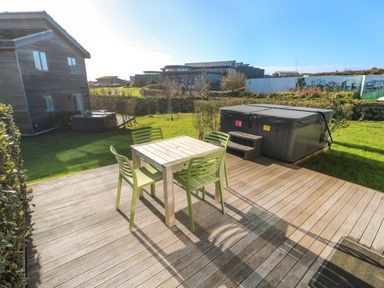 A wooden patio with a table and four chairs next to a hot tub and garden at Una Lodge 77 in Carbis Bay