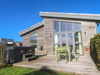 An outdoor patio with a table and four chairs next to a hot tub and a wooden house at Una Lodge 77 in Carbis Bay