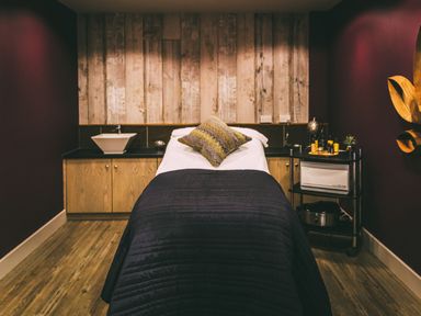 A massage room with a massage table a pillow wooden cabinets and items on a cart at Una Lodge 77 in Carbis Bay