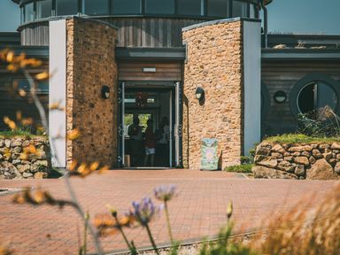 Exterior view of a building entrance with stone walls and people inside at Una Lodge 77 in Carbis Bay