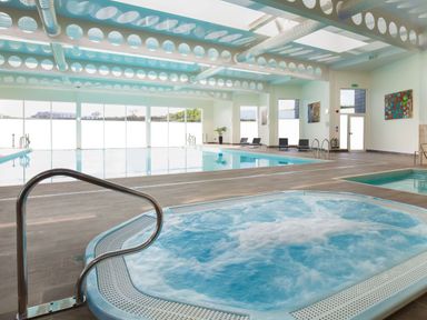 An indoor swimming pool area with a jacuzzi hot tub chairs and large windows at Una Lodge 77 Carbis Bay