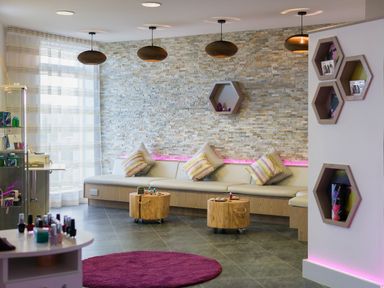 A modern waiting area with a long bench, cushions, round wooden tables on wheels, pendant lights, and a magenta rug at Una Lodge 77 in Carbis Bay