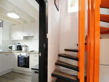 A kitchen with white cabinets and appliances next to an orange spiral staircase at Little Ruffo in Trebarwith near Tintagel