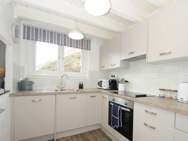 A kitchen with white cabinets and countertops a sink and stove at Little Ruffo in Trebarwith near Tintagel