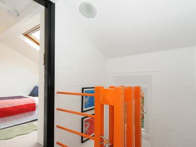 A small landing area with an orange wooden gate and a view into a bedroom with a bed covered in a red and pink blanket at Little Ruffo in Trebarwith near Tintagel