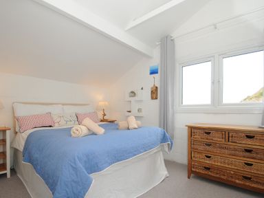 A bedroom with a bed covered in a blue quilt and towels on top next to a wicker dresser and a window at Little Ruffo Trebarwith near Tintagel