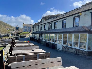 An outdoor seating area with wooden tables and benches beside a two-story building with many windows at Little Ruffo Trebarwith near Tintagel