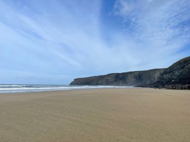 A sandy beach with waves and cliffs in the background at Little Ruffo in Trebarwith near Tintagel