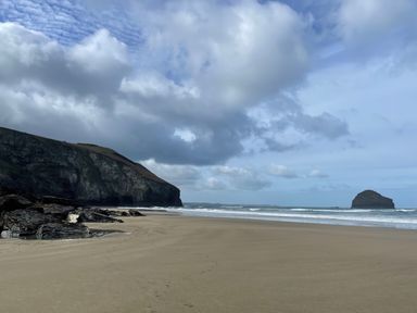 A sandy beach with rocky cliffs on the left and an island in the sea at Little Ruffo in Trebarwith near Tintagel