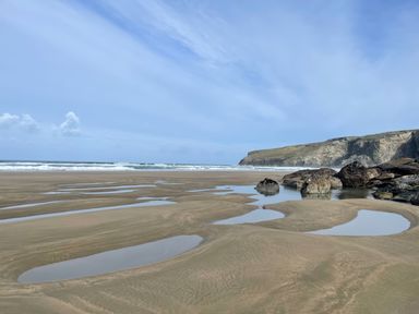 A sandy beach with tidal pools and rocky cliffs in the distance at Little Ruffo Trebarwith near Tintagel