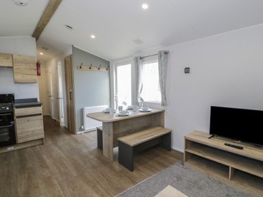 A living room with a table and bench at Lido Silver Plus 111, Prestatyn