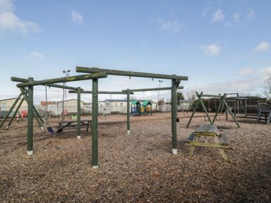 A playground with swings, a slide, and a bench at Lido Silver Plus 111, Prestatyn