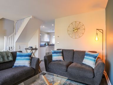 A living room with two gray sofas with blue and white cushions a glass coffee table and a floor lamp at 19 Parc Delfryn in Benllech