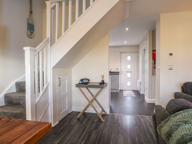 A hallway with stairs, a small table with a vintage phone, and a door leading to another room at 19 Parc Delfryn in Benllech