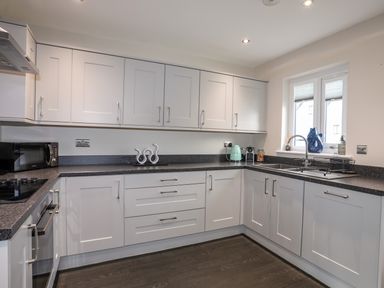 A kitchen with white cabinets a black countertop a microwave kettle and a window at 19 Parc Delfryn in Benllech