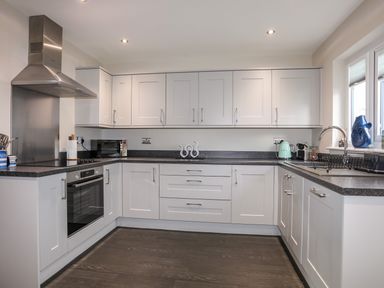 A kitchen with white cabinets black countertops a stainless steel oven and hood a microwave kettle and sink with a window at 19 Parc Delfryn in Benllech