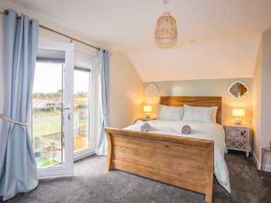 A bedroom with a wooden bed frame blue curtains and bedside tables with lamps at 19 Parc Delfryn in Benllech