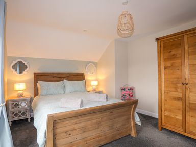 A bedroom with a wooden bed a wooden wardrobe two bedside tables with lamps and a decorative cushion at 19 Parc Delfryn in Benllech