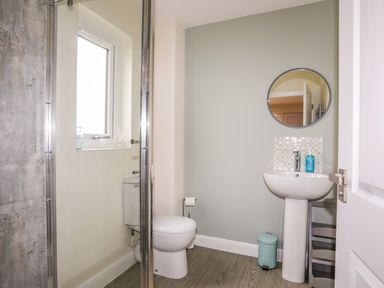A bathroom with a toilet a pedestal sink a round mirror a small window and a shower at 19 Parc Delfryn in Benllech
