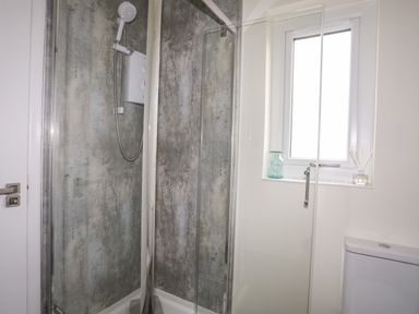 A bathroom with a glass enclosed shower with a wall-mounted shower head and a window with a glass jar and reed diffuser on the sill at 19 Parc Delfryn in Benllech