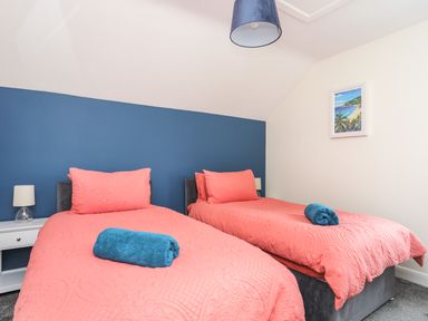 A bedroom with two single beds with coral bedspreads and blue towels on them at 19 Parc Delfryn in Benllech