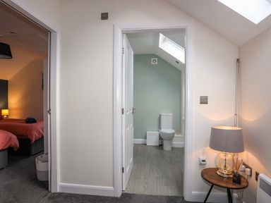 A view of a bathroom with a toilet and skylight and a bedroom with beds and bedside lamp at 19 Parc Delfryn in Benllech