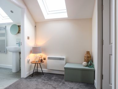 A small corner with a skylight a side table with a lamp and reed diffuser a storage bench with decorative items near a bathroom at 19 Parc Delfryn in Benllech