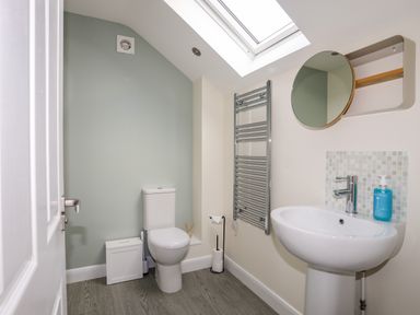 A bathroom with a toilet a pedestal sink a round mirror and a skylight window at 19 Parc Delfryn in Benllech