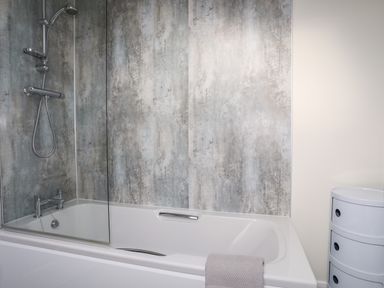 A bathroom with a bathtub shower combination and a white storage unit at 19 Parc Delfryn in Benllech