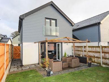 A backyard with patio furniture and a wooden pergola attached to a two-story house at 19 Parc Delfryn in Benllech
