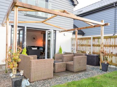 An outdoor patio with wicker chairs and a glass table under a wooden pergola at 19 Parc Delfryn in Benllech