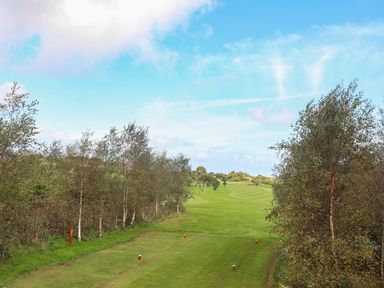 A golf course with trees lining the fairway under a blue sky at 19 Parc Delfryn in Benllech