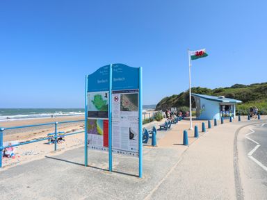 A beachside walkway with Benllech information boards and a Welsh flag near a small blue kiosk at 19 Parc Delfryn in Benllech