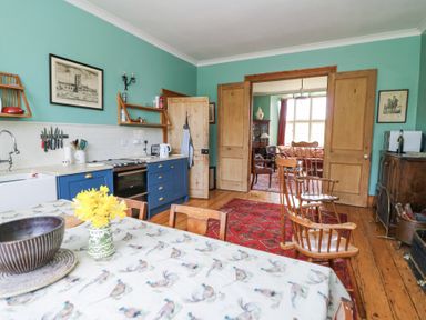 A kitchen with blue cabinets wooden chairs and table with flowers near a living room at Plas Pontfaen near Fishguard and Newport Pembrokeshire