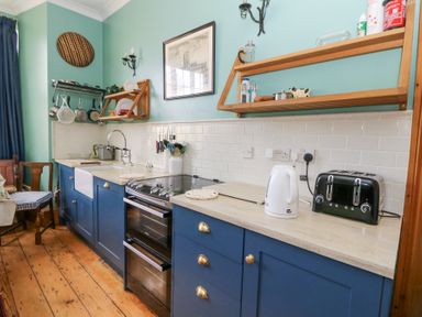 A kitchen with blue cabinets a black oven a white kettle and toaster wooden shelves with kitchen items at Plas Pontfaen near Fishguard and Newport Pembrokeshire