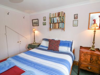 A bedroom with a bed with striped bedding bedside tables with lamps a wall-mounted bookshelf and framed pictures at Plas Pontfaen near Fishguard and Newport Pembrokeshire