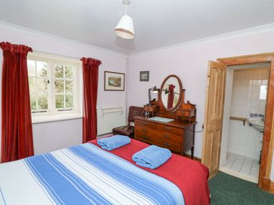 A bedroom with a bed with striped bedding and two blue towels on it with a wooden dresser and mirror near a window with red curtains at Plas Pontfaen near Fishguard and Newport Pembrokeshire