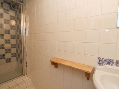 A bathroom with tiled walls a wooden shelf a shower area with patterned tiles and a white sink at Plas Pontfaen near Fishguard and Newport Pembrokeshire