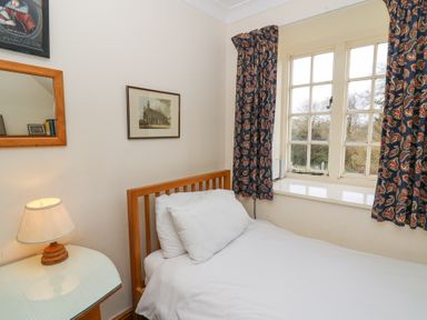 A bedroom with a single bed a wooden headboard a side table with a lamp a window with patterned curtains and framed pictures on the wall at Plas Pontfaen near Fishguard and Newport Pembrokeshire