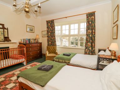 A bedroom with two single beds a crib a chest of drawers an armchair and floral curtains at Plas Pontfaen near Fishguard and Newport Pembrokeshire