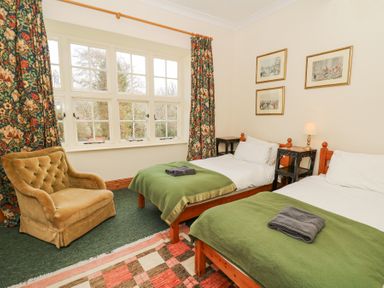 A bedroom with two single beds with green blankets a tufted armchair floral curtains and framed pictures on the wall at Plas Pontfaen near Fishguard and Newport Pembrokeshire