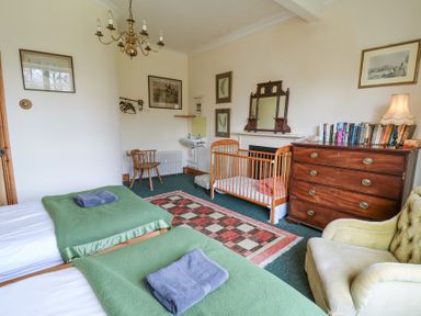 A bedroom with two beds covered with green blankets and folded towels a wooden baby cot a wooden chest of drawers with books and a lamp an armchair and a small sink at Plas Pontfaen near Fishguard and Newport Pembrokeshire