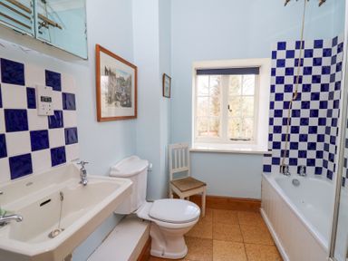 A bathroom with a sink, toilet, bathtub with blue and white tiles, chair, window, and framed pictures on the wall at Plas Pontfaen near Fishguard and Newport Pembrokeshire